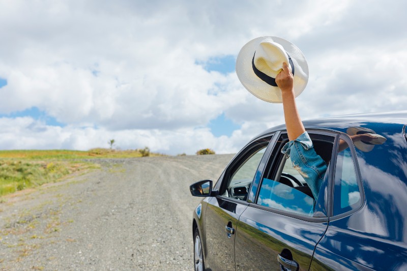 una persona asoma un sombrero de verano por la ventanilla de un coche