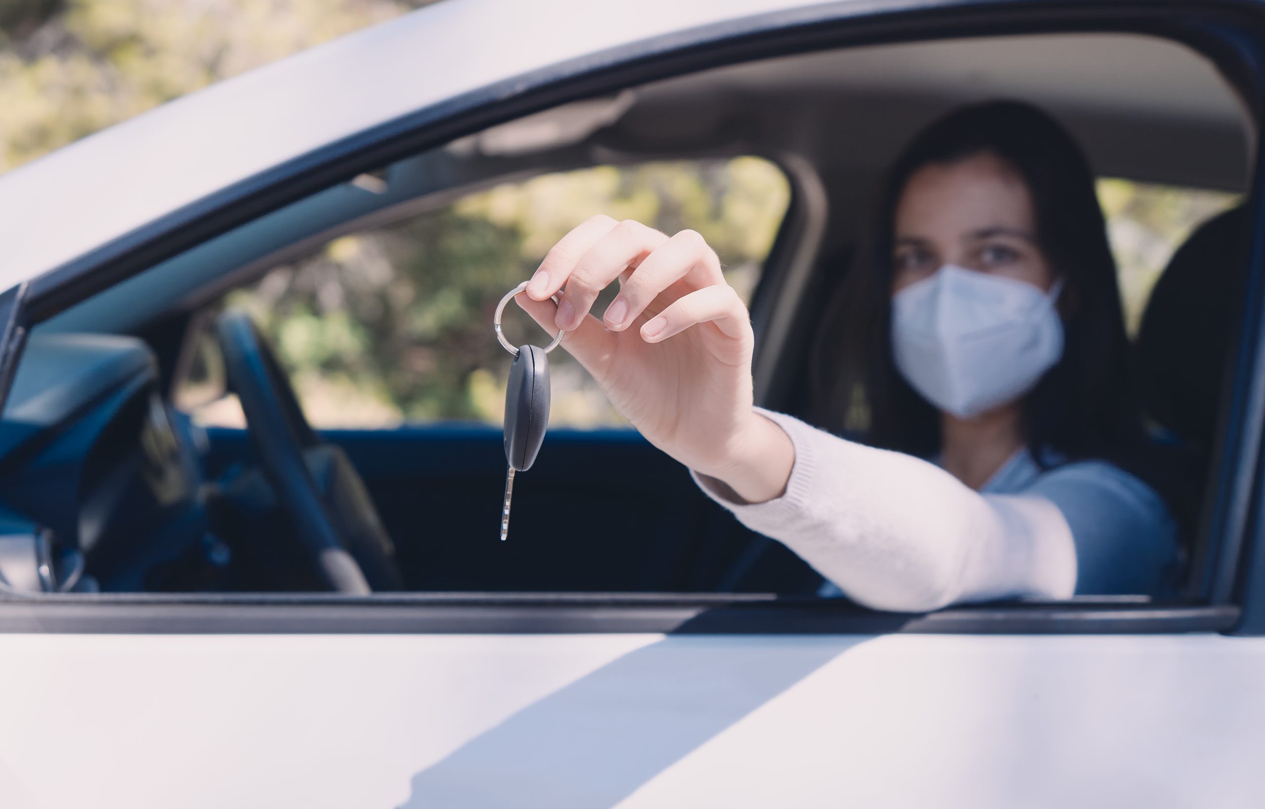 Una mujer con mascarilla entrega las llaves desde el coche